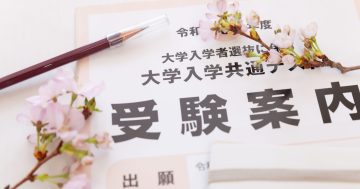 「大学入学共通テスト 受験案内」の書類と鉛筆、桜の花が添えられた写真